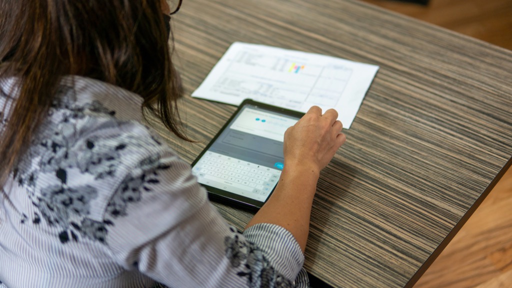 Branchenreport Gesundheitsversorgung 2035 Mitarbeiterin tippt an einem Tisch auf einem Tablet, daneben liegt ein Formular